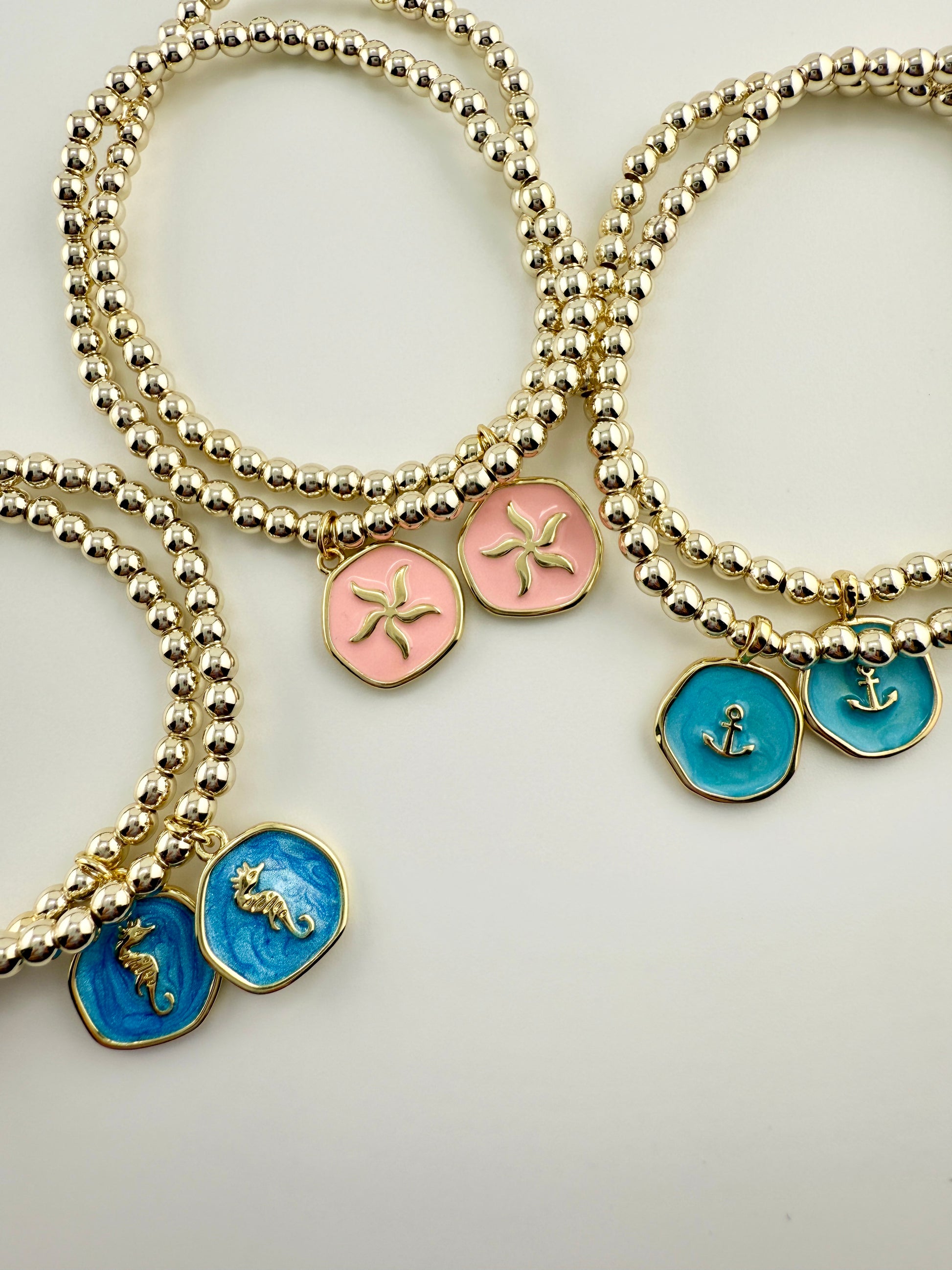 Gold beaded bracelets with colorful charm stones on a light gray background