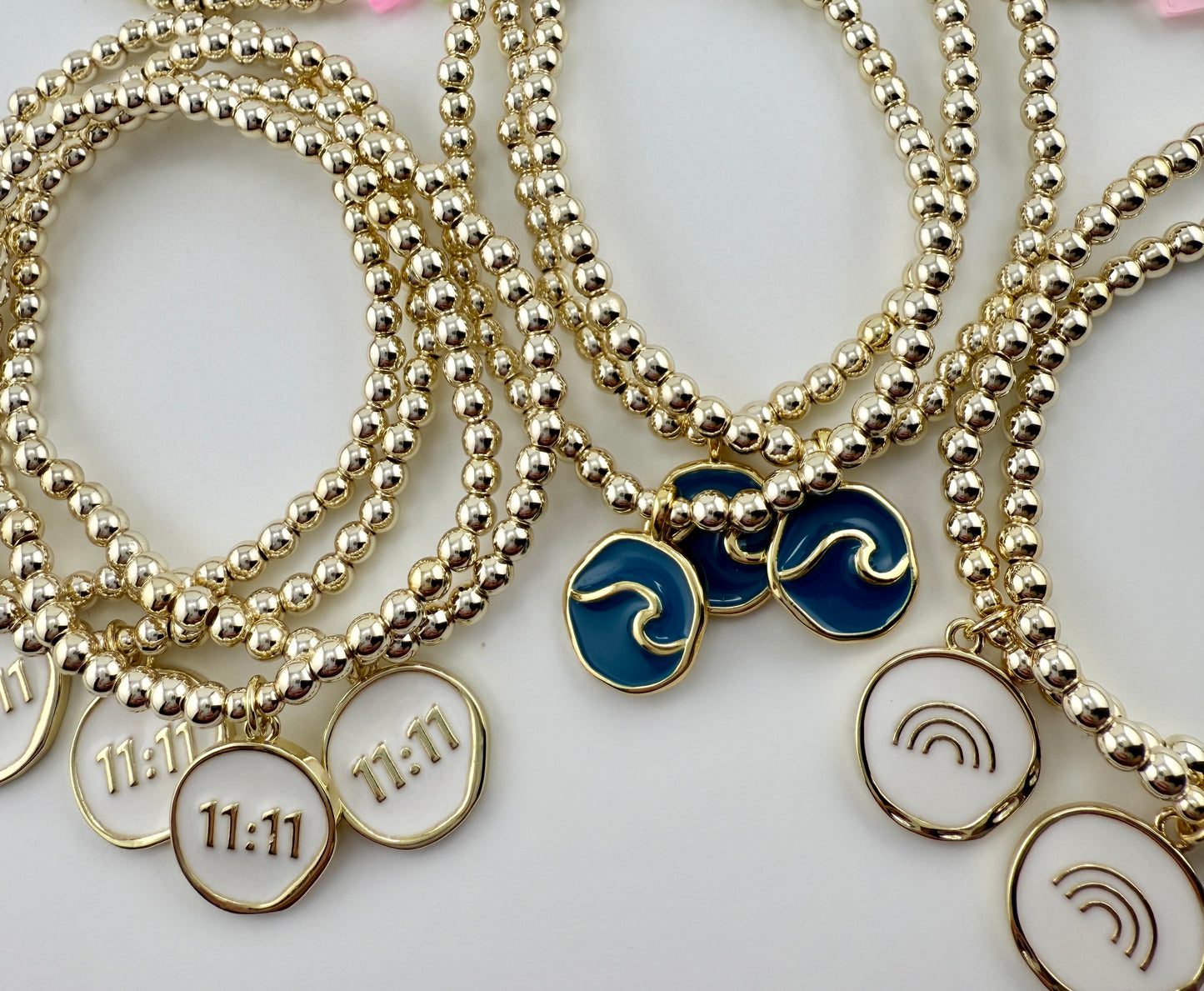 Gold beaded bracelets with wave and symbol charms on a white background
